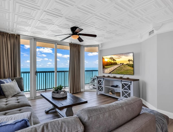 Beachfront living room with ocean view, gray sofas, flat-screen TV, and balcony access